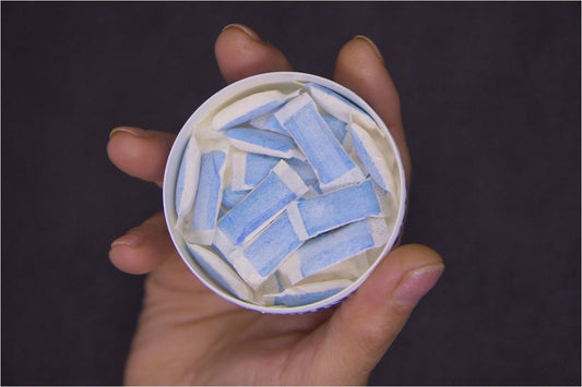 A hand holding an open can filled with blue-and-white nicotine pouches