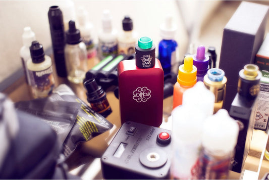 An assortment of vape mods, tanks, and e-liquid bottles arranged on a table