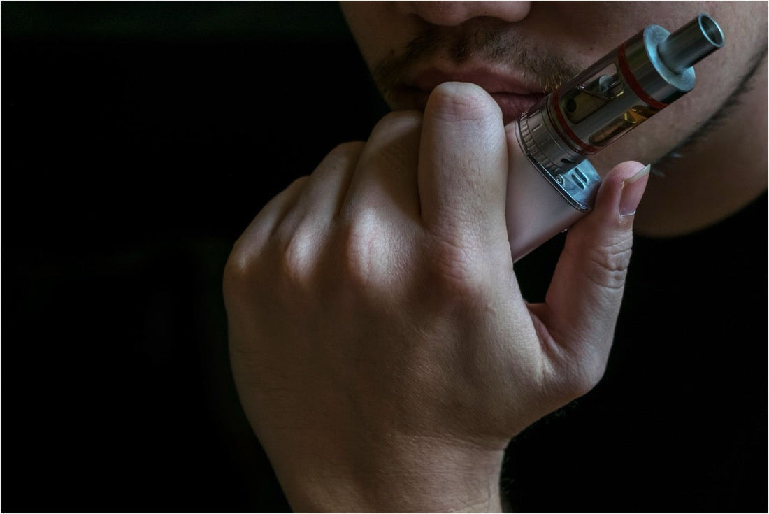 Close-up of a person inhaling from a tank-style vape device against a dark background