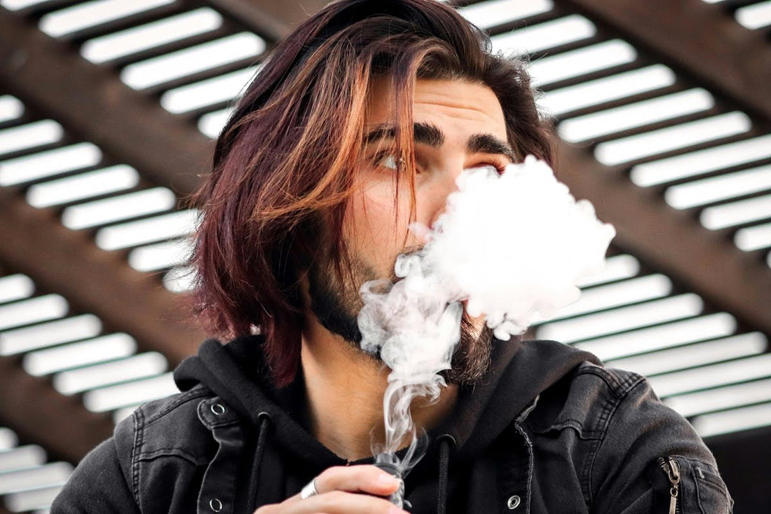 Man exhaling a cloud of vapor while holding a vape device.
