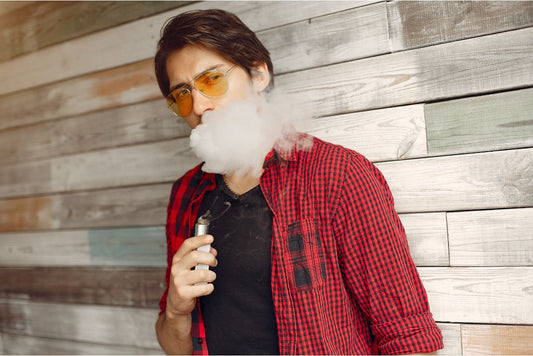 Man in a red plaid shirt and yellow sunglasses, exhaling vapor while holding a vape device
