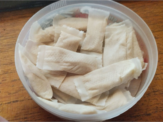 Small white nicotine pouches loose inside a clear plastic tin