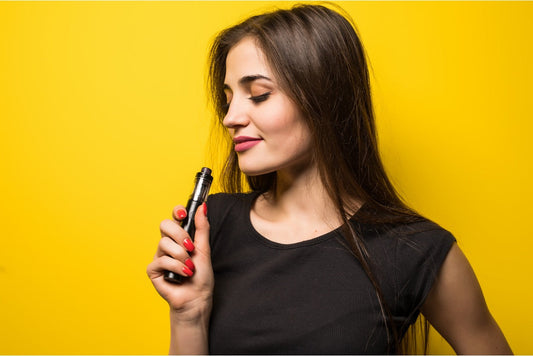 Smiling woman with long dark hair holds a vape pen against a bright yellow background
