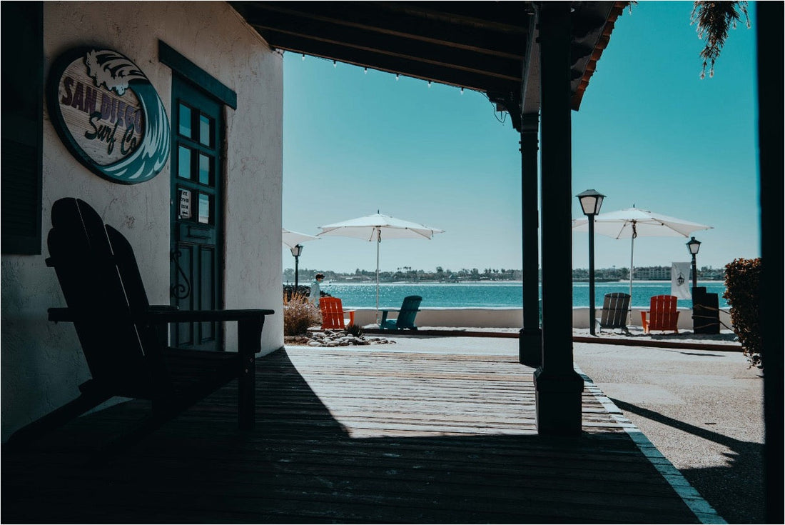 The covered porch of San Diego, looking out toward a beach lined with umbrellas and lounge chairs